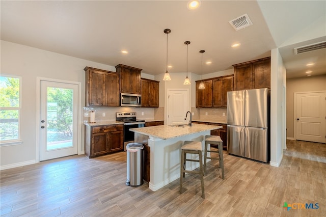 kitchen featuring an island with sink, a breakfast bar area, light stone countertops, stainless steel appliances, and a sink