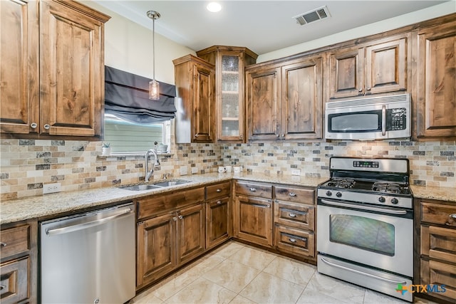 kitchen featuring light stone countertops, glass insert cabinets, a sink, decorative light fixtures, and stainless steel appliances
