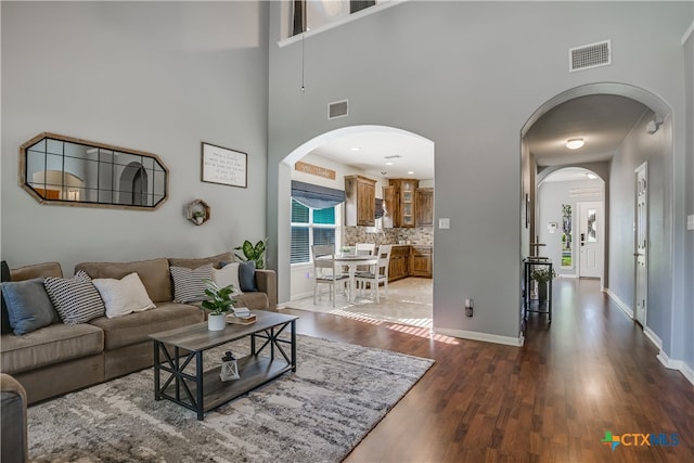 living room featuring arched walkways, dark wood finished floors, and visible vents