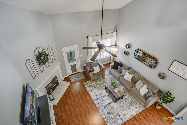 living area featuring wood finished floors, a fireplace, baseboards, a high ceiling, and a ceiling fan
