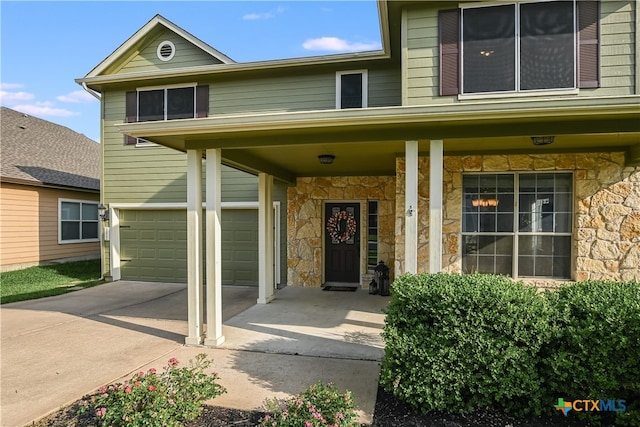 doorway to property with a garage, covered porch, stone siding, and concrete driveway
