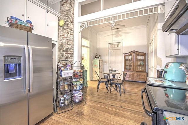 kitchen featuring hardwood / wood-style floors, white cabinetry, a high ceiling, ornamental molding, and stainless steel appliances