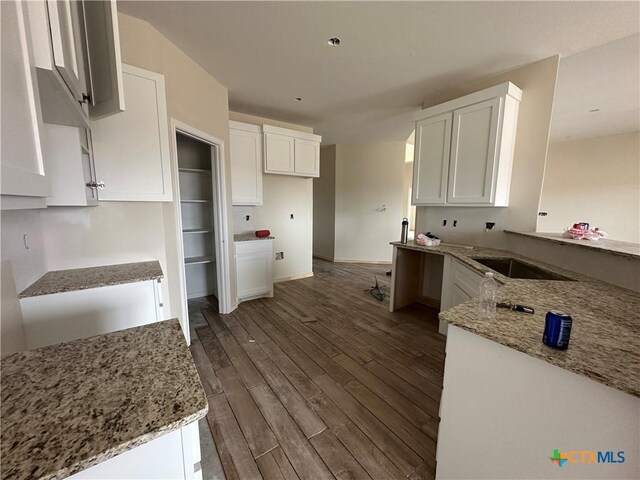 kitchen featuring dark wood-type flooring, white cabinets, light stone counters, and sink