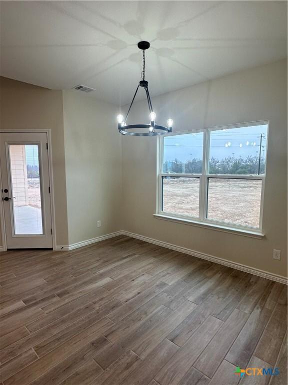 unfurnished dining area featuring a healthy amount of sunlight, an inviting chandelier, and hardwood / wood-style floors