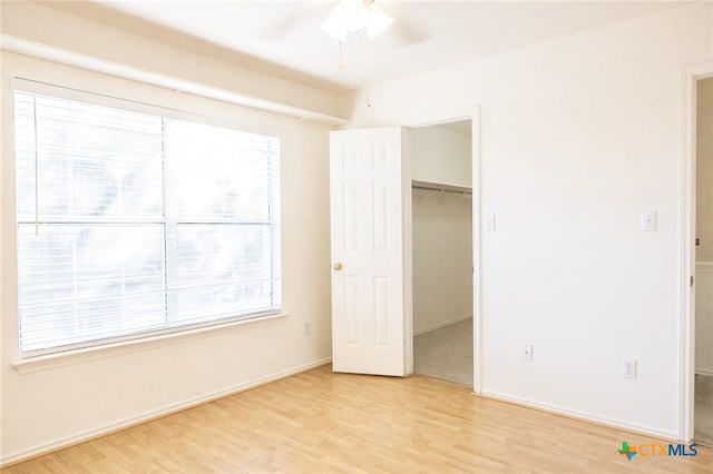 unfurnished bedroom featuring a closet, light wood-type flooring, a walk in closet, and ceiling fan