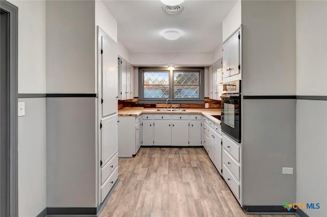 kitchen with white cabinets, sink, oven, and light wood-type flooring