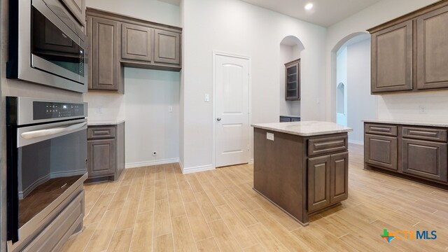 kitchen featuring light wood finished floors, stainless steel appliances, dark brown cabinets, arched walkways, and a center island