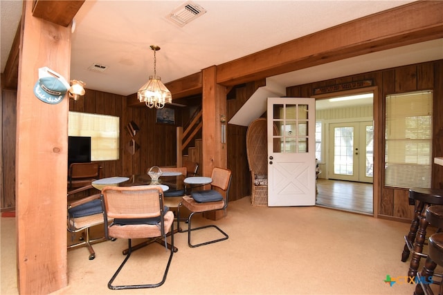 carpeted dining area featuring wooden walls, an inviting chandelier, and french doors