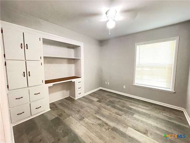 348 N Burke St, Goliad, TX 77963 - unfurnished bedroom with built in study area, a ceiling fan, baseboards, and dark wood-type flooring