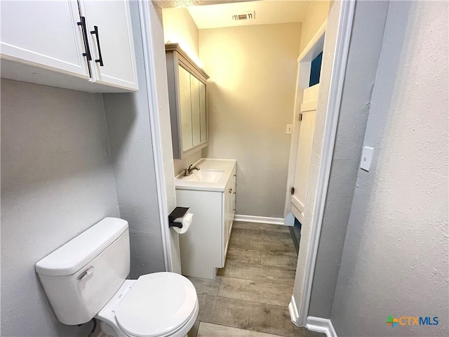 348 N Burke St, Goliad, TX 77963 - half bath with visible vents, wood finished floors, vanity, baseboards, and toilet
