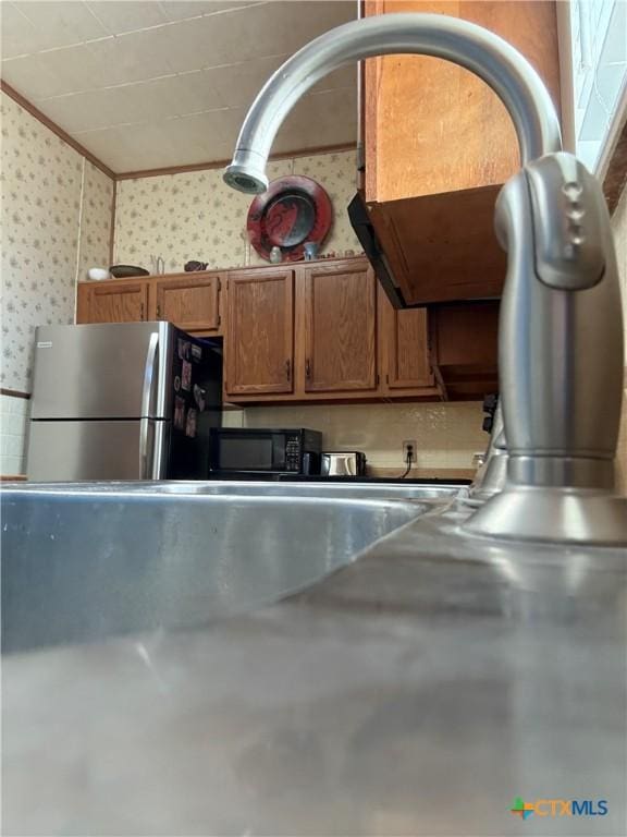 202 S Virginia St, Port Lavaca, TX 77979 - kitchen with wallpapered walls, freestanding refrigerator, crown molding, black microwave, and brown cabinetry