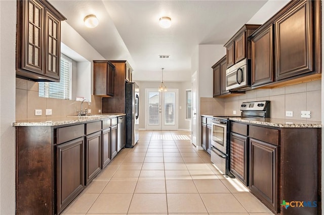 kitchen with dark brown cabinets, backsplash, light tile patterned floors, appliances with stainless steel finishes, and a sink