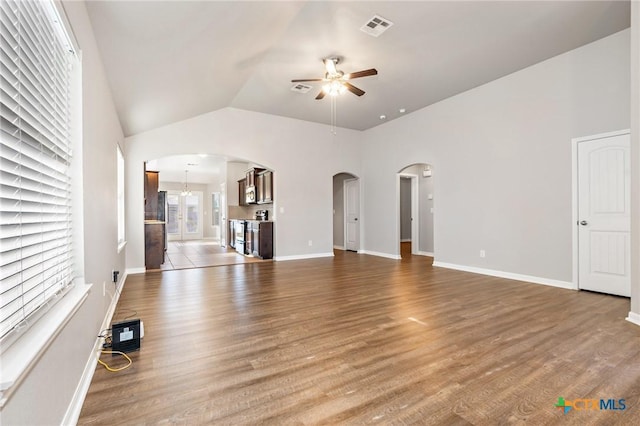 unfurnished living room with visible vents, baseboards, ceiling fan with notable chandelier, wood finished floors, and arched walkways