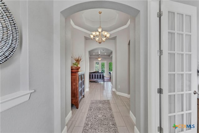 hall with a raised ceiling, ornamental molding, and an inviting chandelier