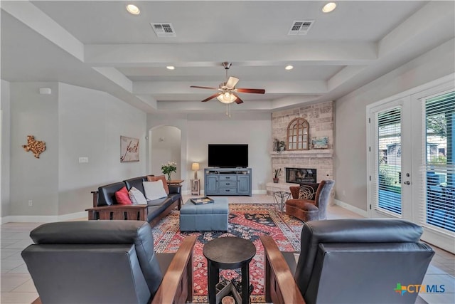 living room with beamed ceiling, light tile patterned floors, a stone fireplace, and ceiling fan