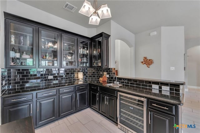 bar with sink, hanging light fixtures, beverage cooler, dark stone countertops, and decorative backsplash