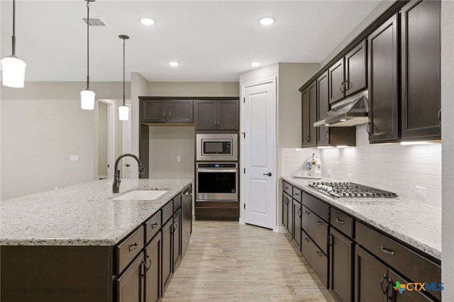 kitchen featuring stainless steel appliances, decorative light fixtures, light stone countertops, sink, and a kitchen island with sink