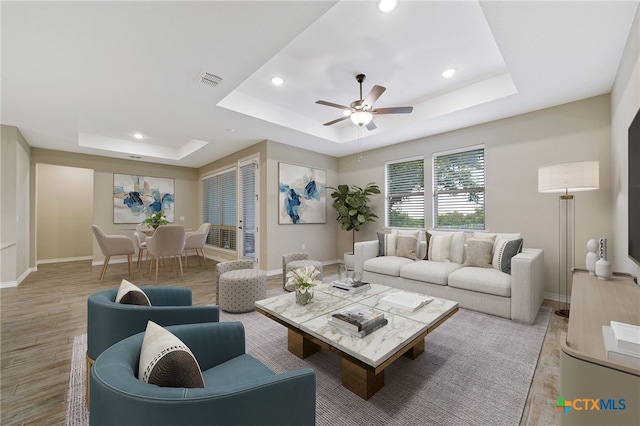 living room featuring light hardwood / wood-style flooring, ceiling fan, and a tray ceiling