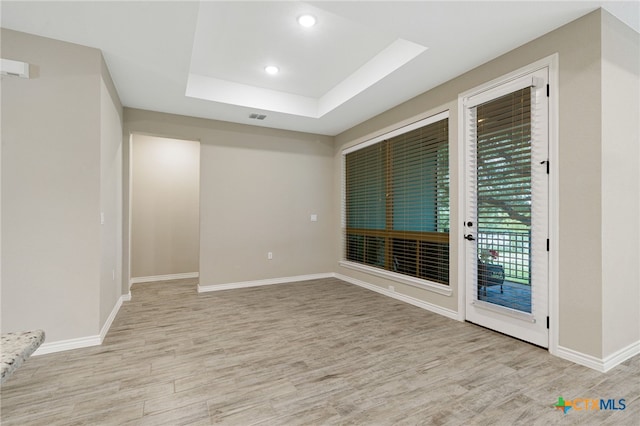 empty room with light hardwood / wood-style flooring and a tray ceiling