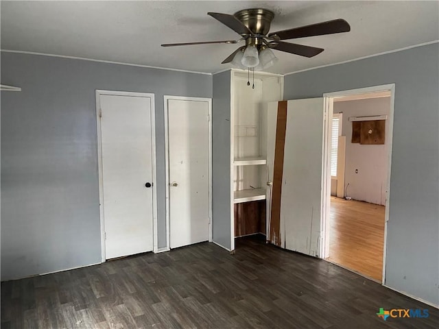 unfurnished bedroom with ceiling fan, ensuite bathroom, dark wood-type flooring, and multiple closets