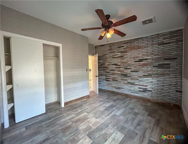 unfurnished bedroom featuring brick wall, dark hardwood / wood-style floors, a closet, and ceiling fan