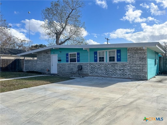 view of front of house with driveway, brick siding, and fence