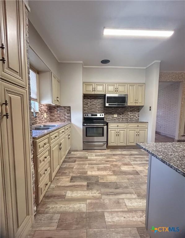 3101 Bobolink Ln, Victoria, TX 77901 - kitchen featuring stainless steel appliances, cream cabinetry, decorative backsplash, light wood-type flooring, and ornamental molding