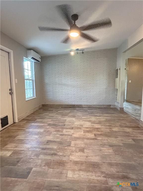 empty room featuring ceiling fan, brick wall, a wall mounted air conditioner, and hardwood / wood-style flooring