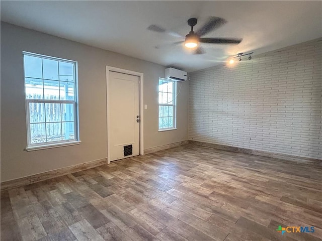 empty room featuring hardwood / wood-style floors, ceiling fan, a wall mounted AC, and brick wall