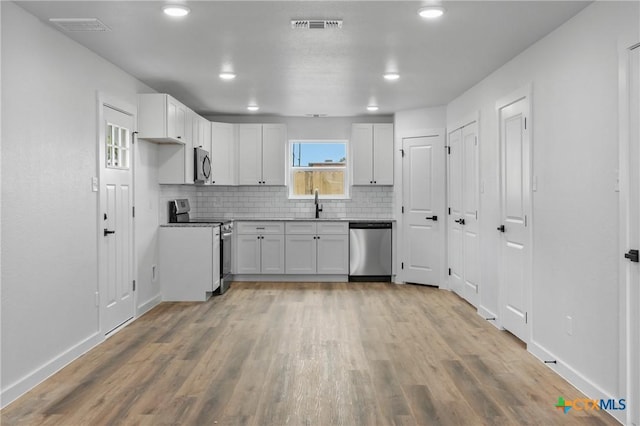 kitchen with backsplash, white cabinets, sink, light hardwood / wood-style flooring, and stainless steel appliances