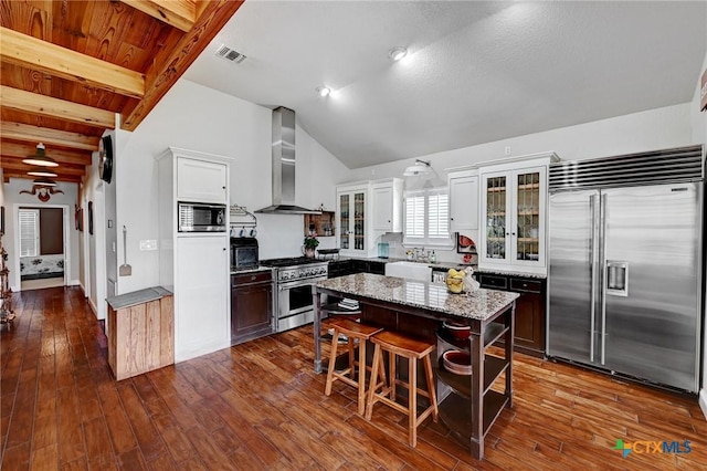 kitchen with visible vents, vaulted ceiling with beams, wall chimney range hood, dark wood finished floors, and built in appliances