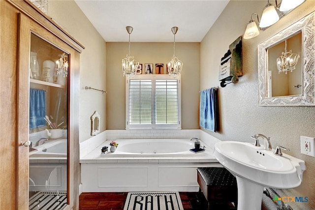 full bath featuring a notable chandelier, a jetted tub, and a textured wall