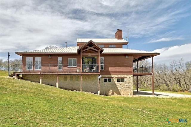 back of property with stone siding, a yard, metal roof, a balcony, and a chimney