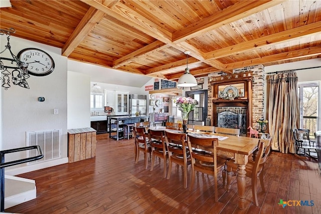 dining room with visible vents, dark wood finished floors, beam ceiling, wooden ceiling, and a brick fireplace