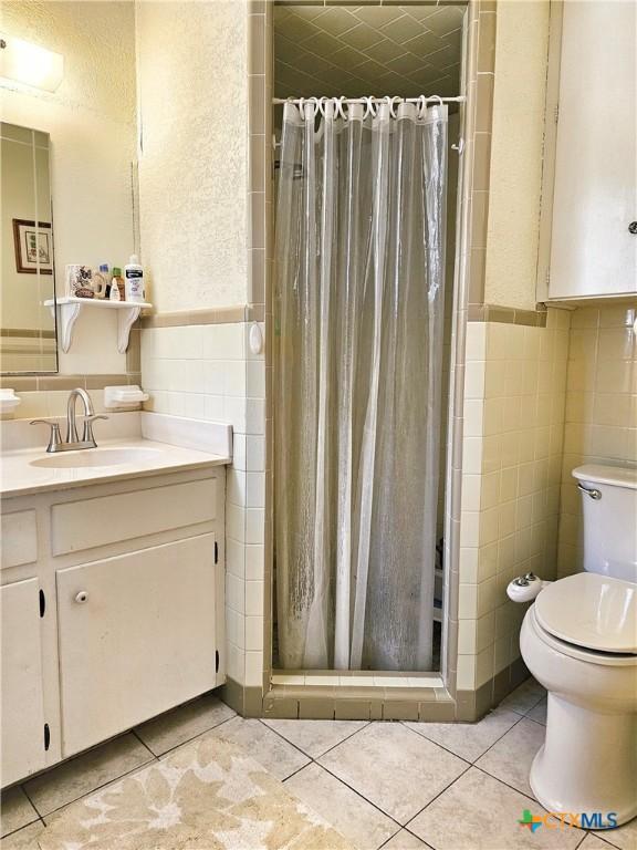 bathroom with toilet, a shower with curtain, tile patterned floors, and tile walls