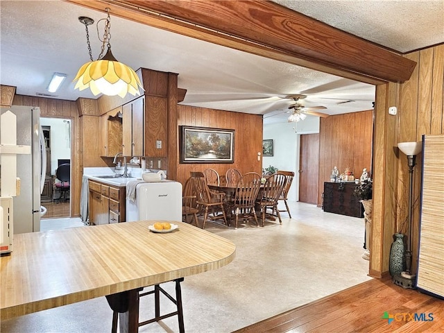 dining area with wooden walls, ceiling fan, light colored carpet, and a textured ceiling