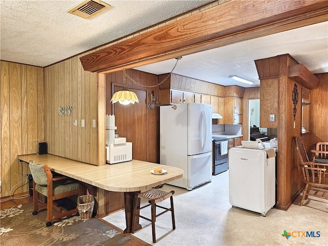 kitchen featuring a textured ceiling, white fridge, stainless steel electric range oven, and wood walls