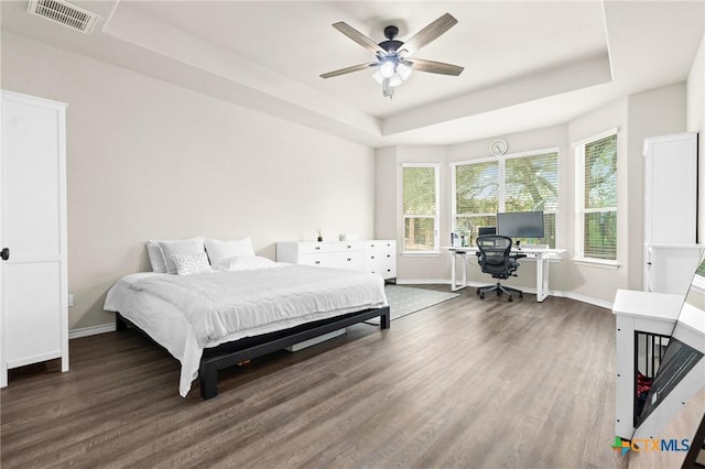 bedroom with baseboards, a tray ceiling, visible vents, and wood finished floors
