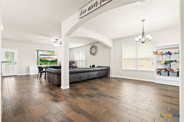 living area featuring dark wood-style flooring, arched walkways, baseboards, and ceiling fan with notable chandelier