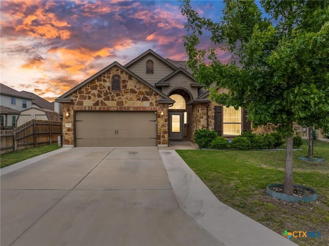 french country inspired facade featuring fence, an attached garage, a front lawn, stone siding, and concrete driveway