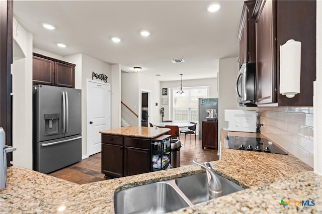 kitchen with dark wood-style flooring, dark brown cabinets, a center island, tasteful backsplash, and appliances with stainless steel finishes