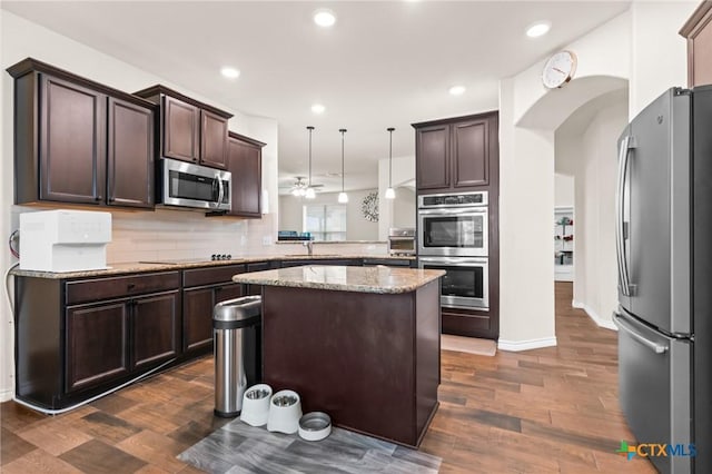 kitchen featuring dark brown cabinetry, appliances with stainless steel finishes, a sink, arched walkways, and dark wood-style floors