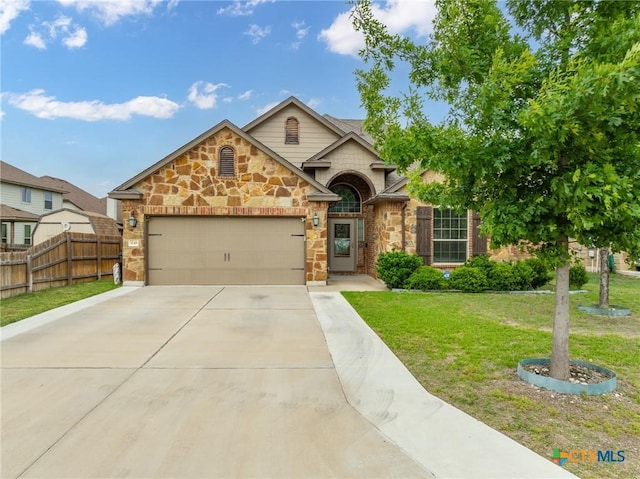 view of front facade featuring fence, an attached garage, stone siding, a front yard, and driveway
