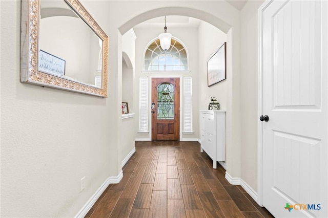 entrance foyer featuring baseboards, dark wood-style flooring, and arched walkways