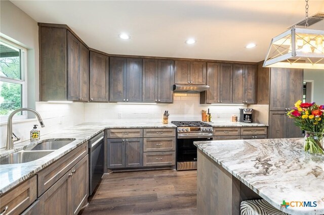 kitchen featuring light stone countertops, a sink, dark wood finished floors, stainless steel appliances, and under cabinet range hood