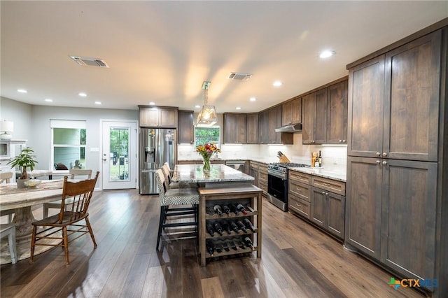 kitchen featuring appliances with stainless steel finishes, light stone countertops, under cabinet range hood, and visible vents