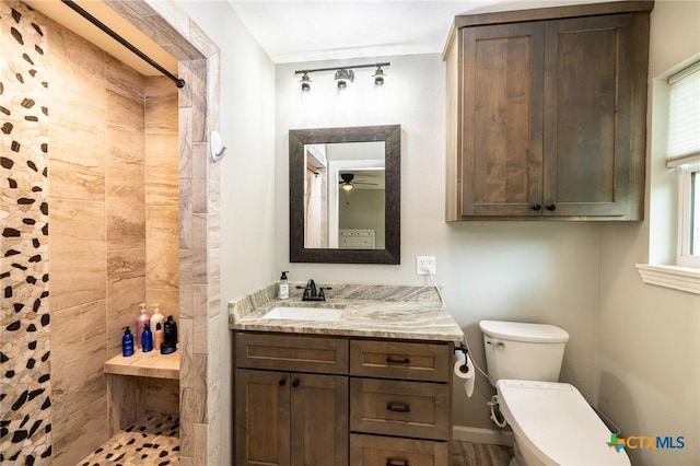 bathroom featuring vanity, a ceiling fan, a tile shower, and toilet