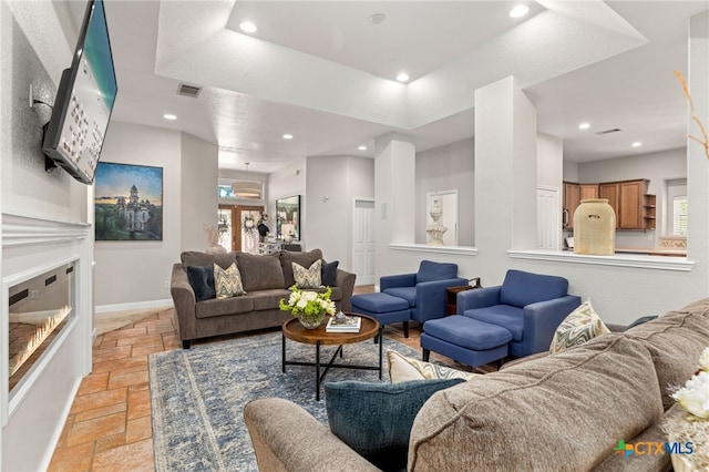living area with a glass covered fireplace, stone tile flooring, recessed lighting, and visible vents