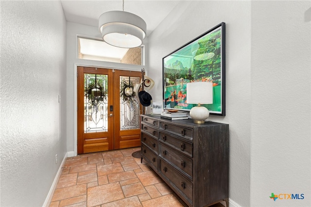foyer entrance with baseboards, french doors, a textured wall, and stone tile floors