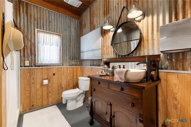bathroom with concrete floors, toilet, vanity, visible vents, and wooden walls
